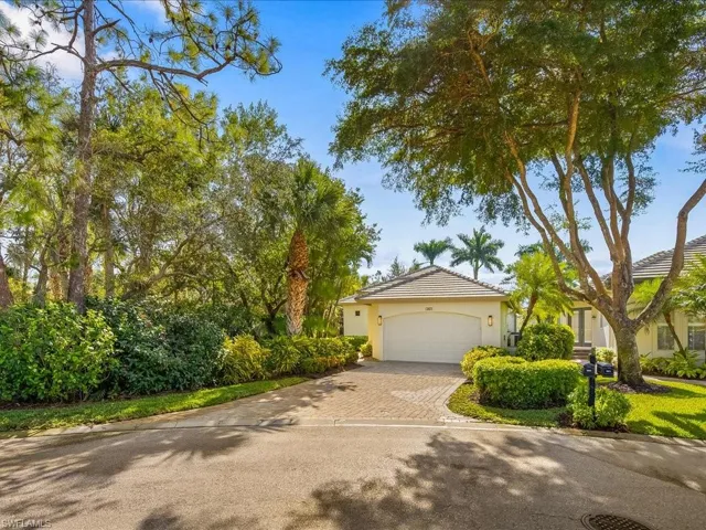 View of property hidden behind natural elements with driveway, a tile roof, an attached garage, and stucco siding