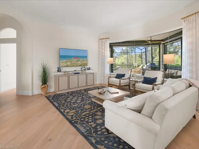 Living room with arched walkways, light wood-type flooring, and crown molding