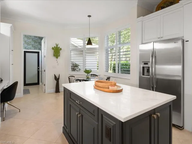 Kitchen featuring stainless steel fridge with ice dispenser, hanging light fixtures, ornamental molding, light stone countertops, and a center island
