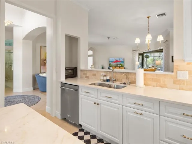 Kitchen with a chandelier, backsplash, light stone countertops, dishwasher, and white cabinets