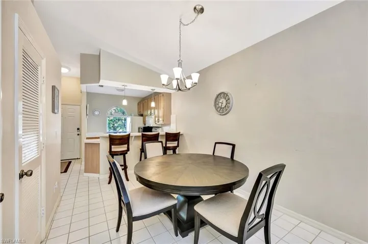 Vaulted ceiling dining area featuring tile flooring and a chandelier, with a kitchen pass-through and breakfast bar in the background