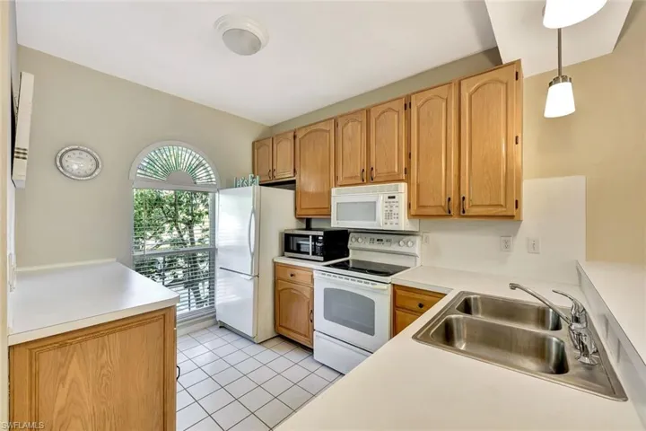 Kitchen featuring white countertops, light wood-finish cabinetry, a double basin stainless steel sink, and a large arched window with blinds
