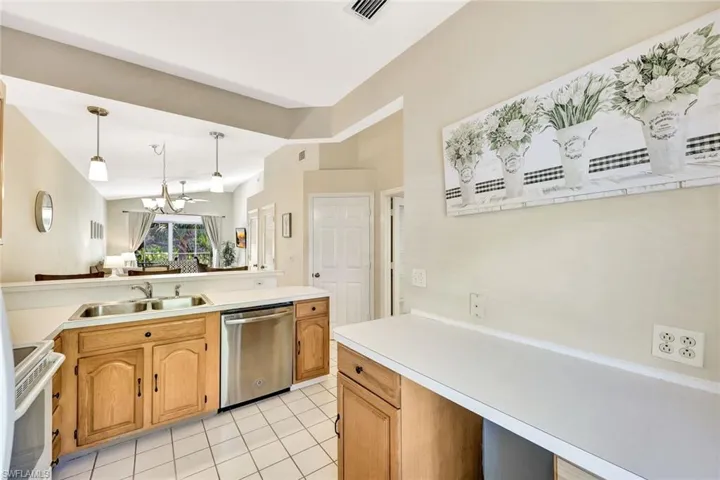 Well-lit kitchen featuring light wood-finish cabinetry, white countertops, a stainless steel dishwasher, and a double basin sink
