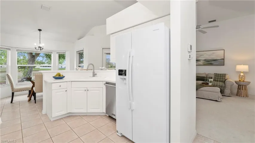 Kitchen featuring white fridge with ice dispenser, vaulted ceiling, suspended lighting, a peninsula, and white cabinetry