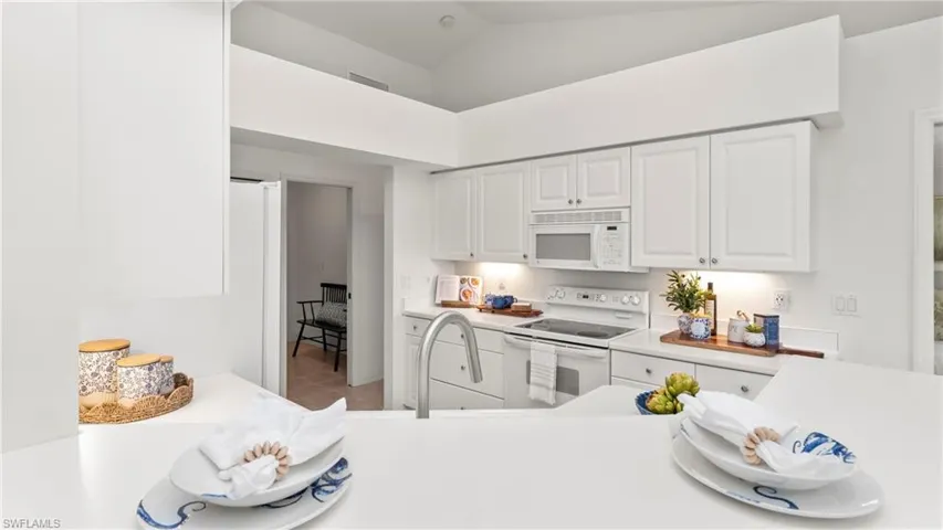 Kitchen featuring light countertops, white cabinets, white appliances, and vaulted ceiling