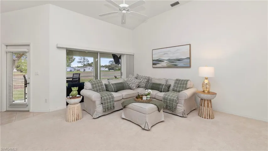 Living area with a ceiling fan, light carpet, and vaulted ceiling