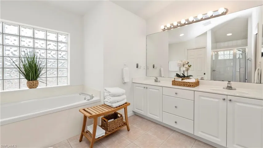 Bathroom with double vanity, a garden tub, light tile patterned flooring, a stall shower, and lofted ceiling