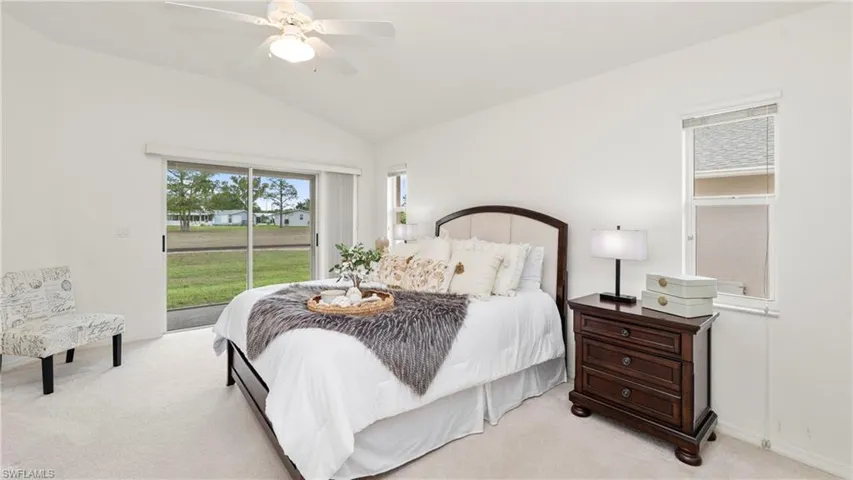 Carpeted bedroom featuring access to outside, vaulted ceiling, and ceiling fan