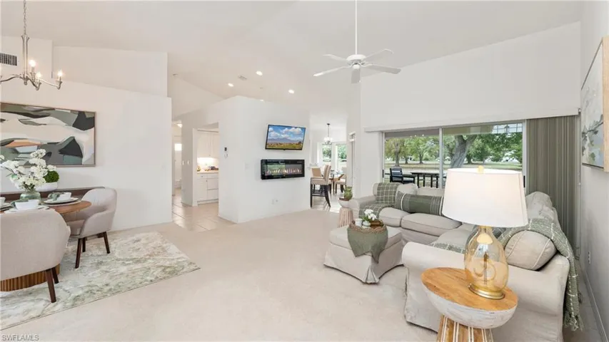 Living room featuring suspended lighting, light carpet, a ceiling fan, and vaulted ceiling