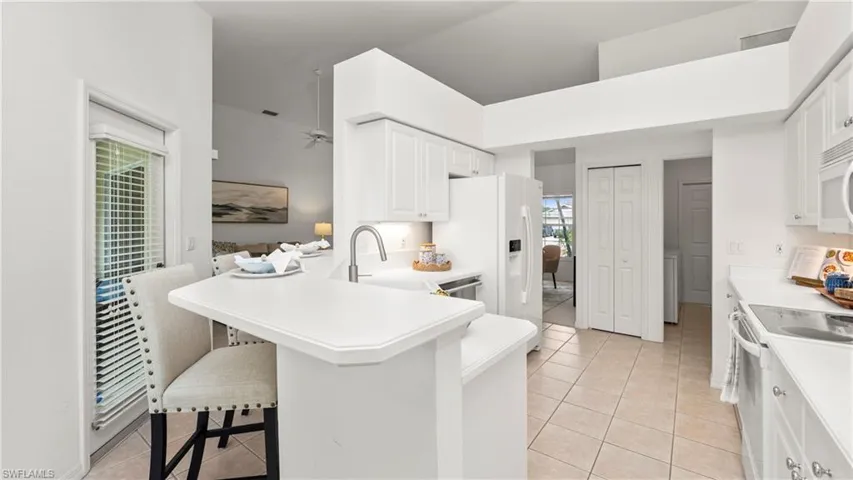 Kitchen featuring white appliances, light countertops, light tile patterned floors, white cabinets, and a peninsula