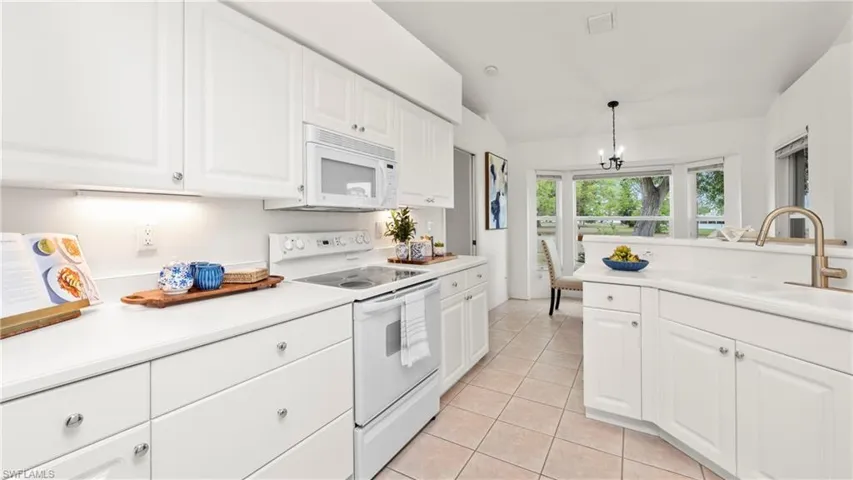 Kitchen with white appliances, light countertops, white cabinetry, and vaulted ceiling
