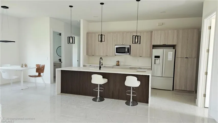 Kitchen featuring hanging light fixtures, light brown cabinetry, white refrigerator with ice dispenser, modern cabinets, and light stone countertops
