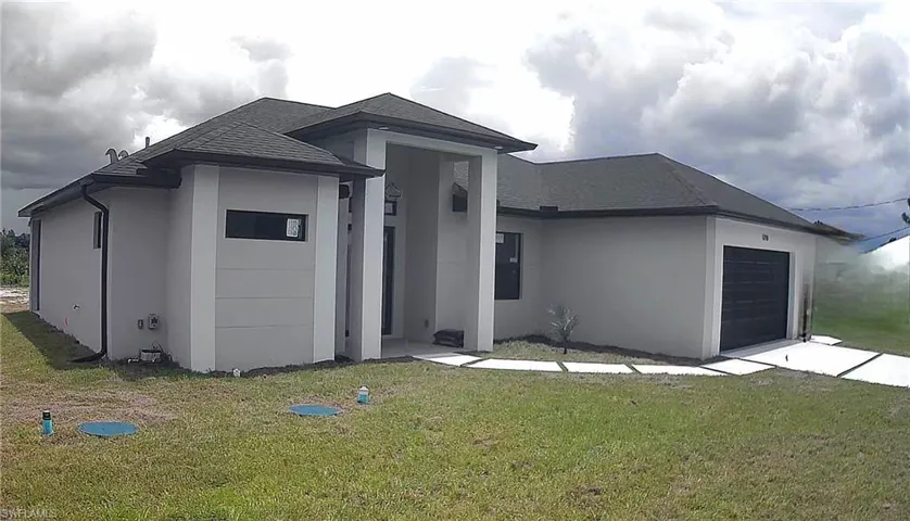 View of front of house with a shingled roof, a garage, stucco siding, a front lawn, and driveway
