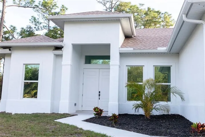 Entrance to property featuring a shingled roof and stucco siding