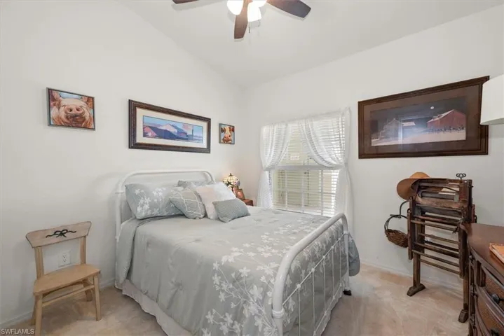 Second bedroom with a lofted ceiling, ceiling fan, and light neutral carpeting.