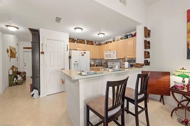 Bright and functional kitchen with white appliances, light cabinetry, and Corian style hard surface countertops, complemented by a convenient breakfast bar for casual dining.