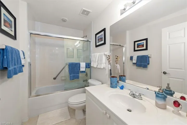 Full bathroom featuring a tub and shower with glass door, vanity, and light patterned tile flooring.