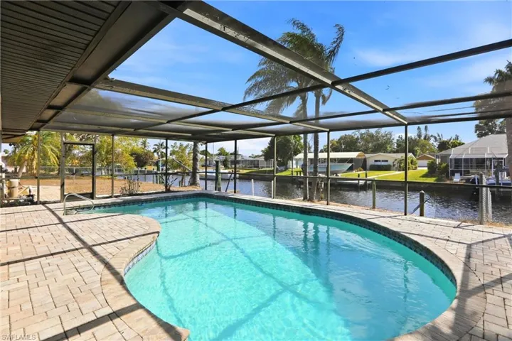 Swimming pool featuring glass enclosure, a dock, a water view, boat lift, and a sunroom
