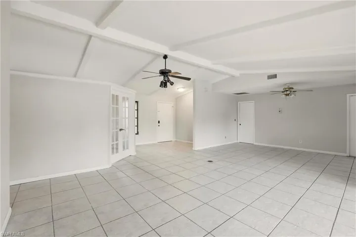 Unfurnished room featuring a ceiling fan, light tile patterned floors, and beamed ceiling
