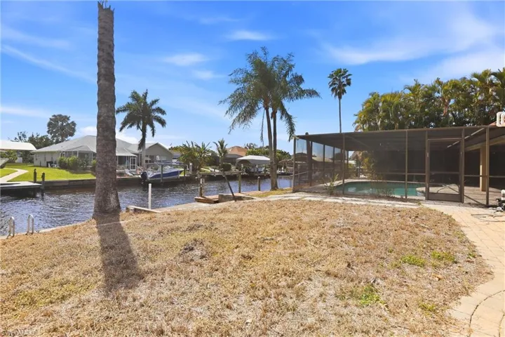 View of green lawn featuring a water view, a boat dock, a sunroom, an outdoor pool, and a residential view
