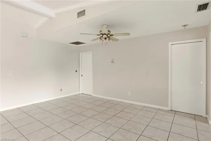 Empty room featuring ceiling fan, vaulted ceiling with beams, and light tile patterned floors