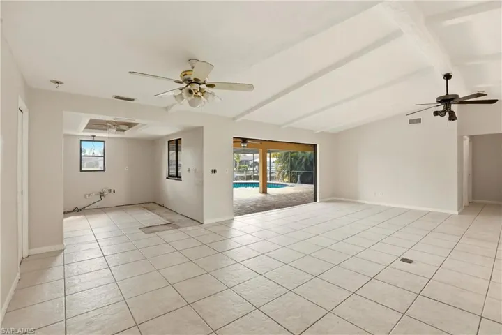 Empty room featuring a ceiling fan, beam ceiling, and light tile patterned floors