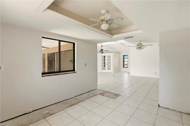 Unfurnished room featuring a tray ceiling, light tile patterned flooring, and ceiling fan