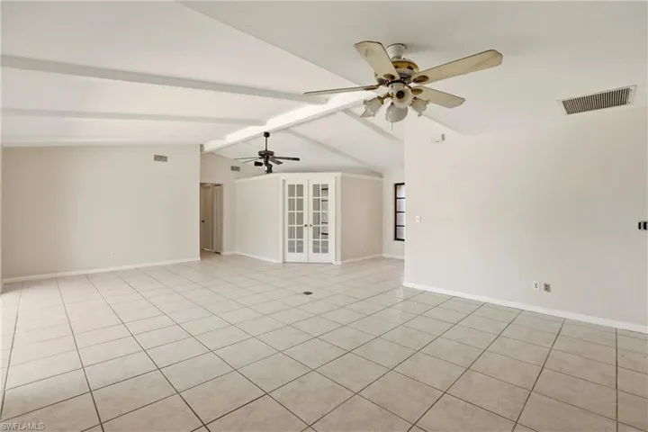 Empty room featuring french doors, beam ceiling, light tile patterned flooring, and a ceiling fan