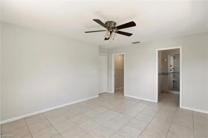 Unfurnished bedroom featuring a walk in closet, ceiling fan, light tile patterned floors, and ensuite bath