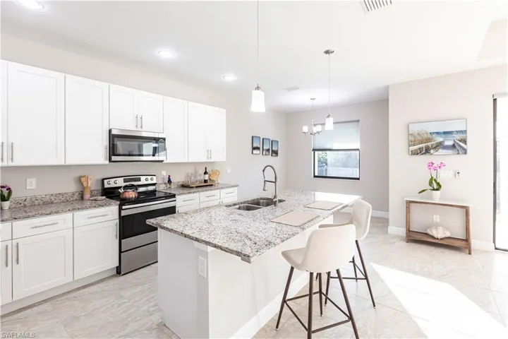 Kitchen with a kitchen island with sink, sink, white cabinetry, and appliances with stainless steel finishes