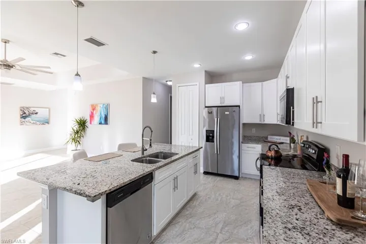 Kitchen with white cabinets, sink, hanging light fixtures, and black appliances