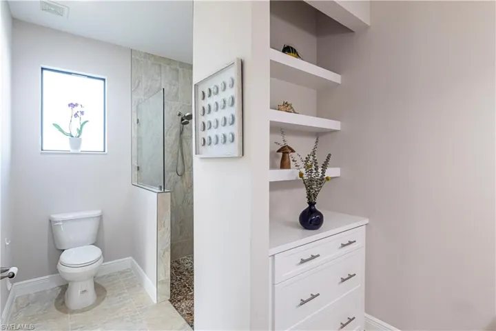 Bathroom with built in shelves, toilet, and tiled shower