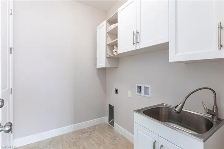 Clothes washing area featuring electric dryer hookup, sink, hookup for a washing machine, and cabinets