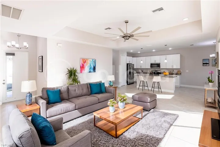 *virtual staging* Tiled living room with ceiling fan with notable chandelier and a raised ceiling