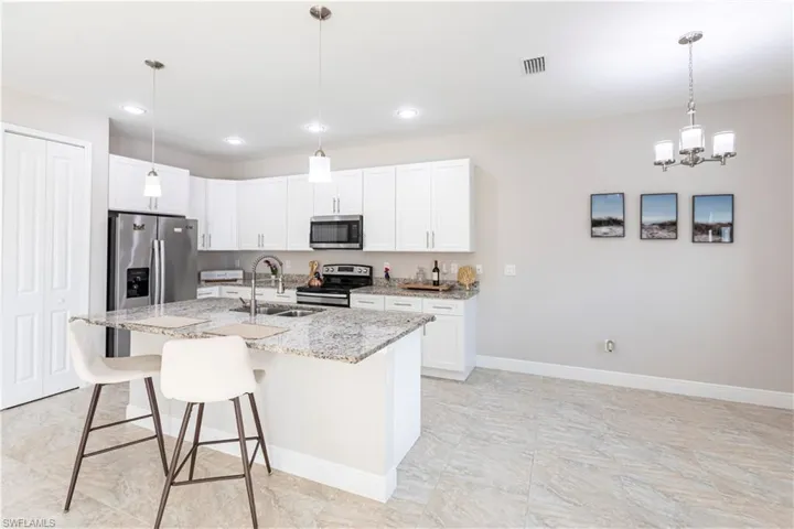 Kitchen with appliances with stainless steel finishes, white cabinetry, sink, light stone counters, and a center island with sink