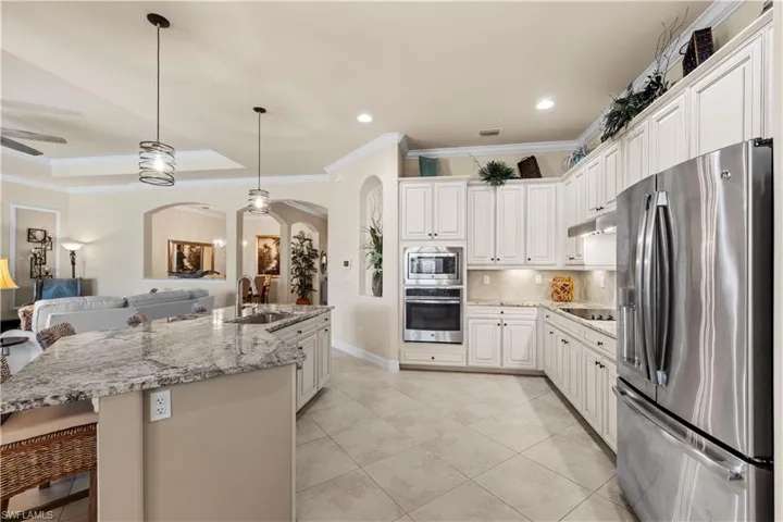 Kitchen with arched walkways, appliances with stainless steel finishes, a sink, open floor plan, and crown molding
