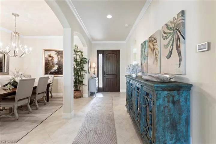 Entrance foyer featuring an inviting chandelier, light 20" tile flooring, crown molding, baseboards, and arched walkways