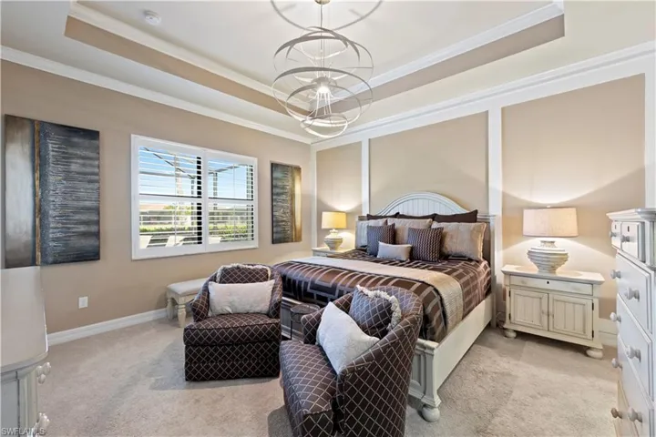 Bedroom with light colored carpet, a raised ceiling, and ornamental molding