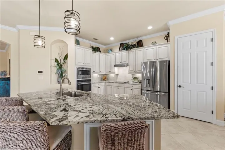 Kitchen featuring a sink, under cabinet range hood, a breakfast bar area, white cabinetry, and appliances with stainless steel finishes