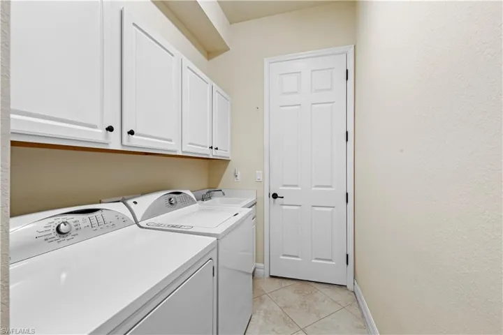Washroom with cabinet space, washing machine and clothes dryer, a sink, baseboards, and light 20" tile flooring