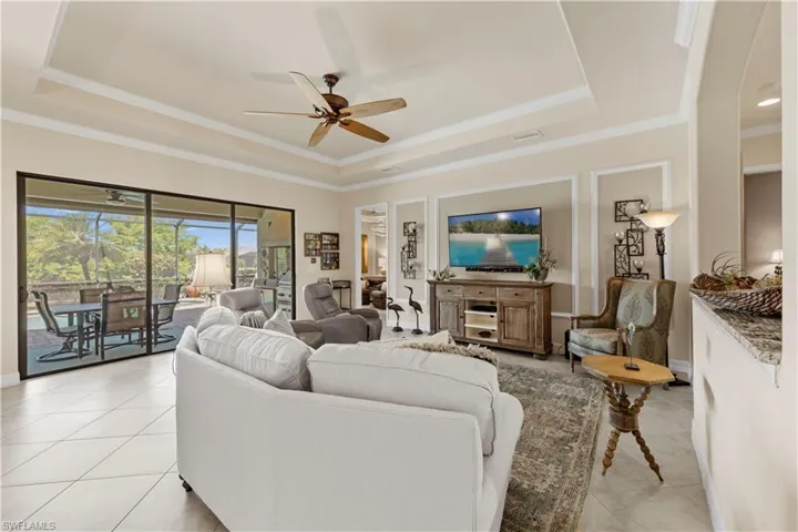 Living area featuring arched walkways, light 20" tile floors, ceiling fan, a raised ceiling, and crown molding