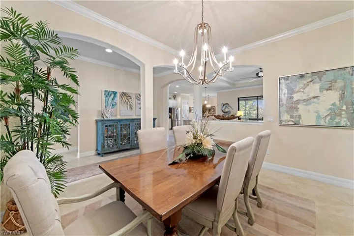 Dining space with light 20" tile floors, crown molding, baseboards, arched walkways, and ceiling fan with notable chandelier