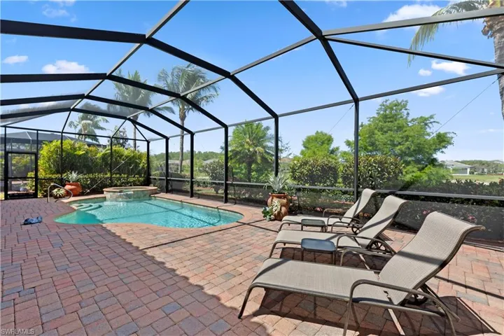 View of pool featuring glass enclosure, a pool with connected hot tub, and a patio area