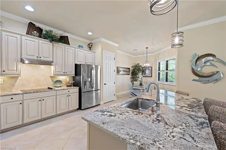 Kitchen featuring a sink, under cabinet range hood, light stone countertops, black electric cooktop, and stainless steel fridge with ice dispenser