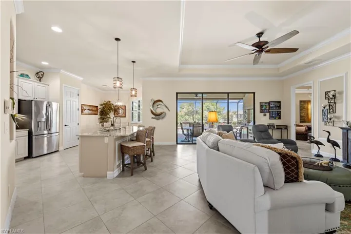 Living area featuring light 20" tile flooring, a raised ceiling, a ceiling fan, and crown molding