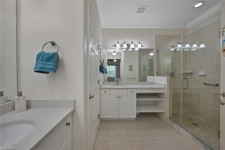 Full bathroom with two vanities, tile patterned flooring, a stall shower, and crown molding