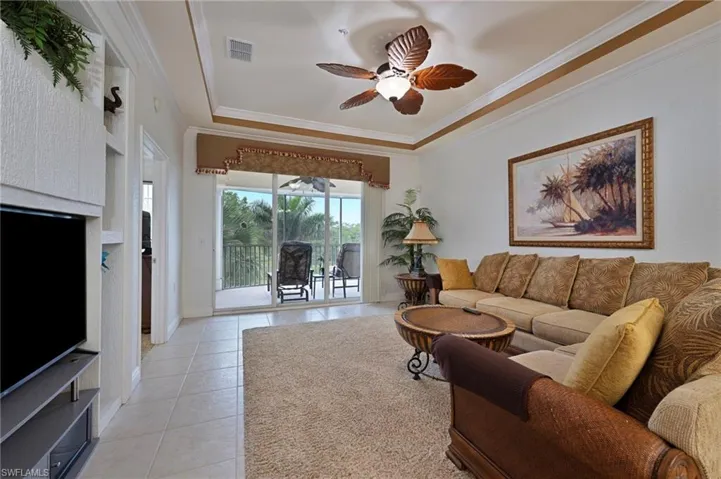 Living area with a tray ceiling, light tile patterned floors, ceiling fan, and crown molding