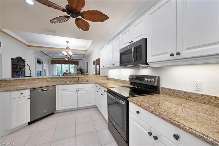Kitchen with stainless steel dishwasher, range with electric cooktop, a tray ceiling, a chandelier, and ornamental molding