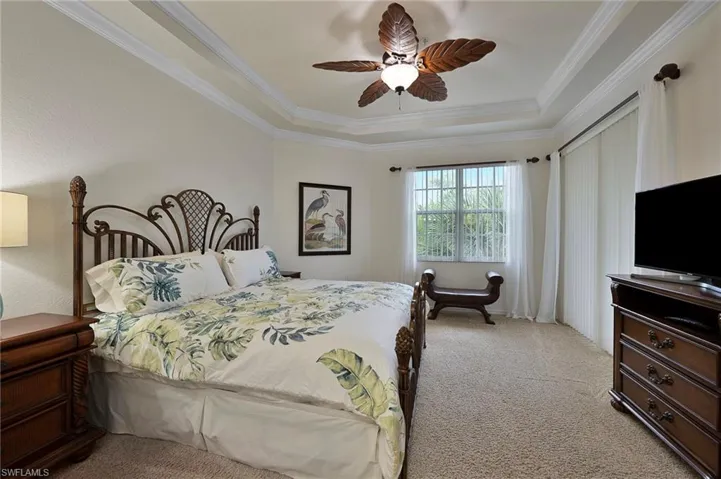 Carpeted bedroom with a tray ceiling, ornamental molding, and a ceiling fan