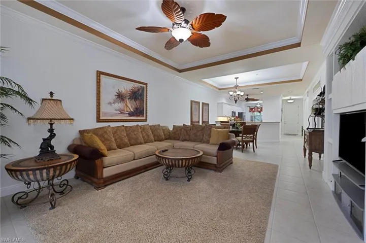 Living area with a tray ceiling, light tile patterned flooring, crown molding, a chandelier, and ceiling fan